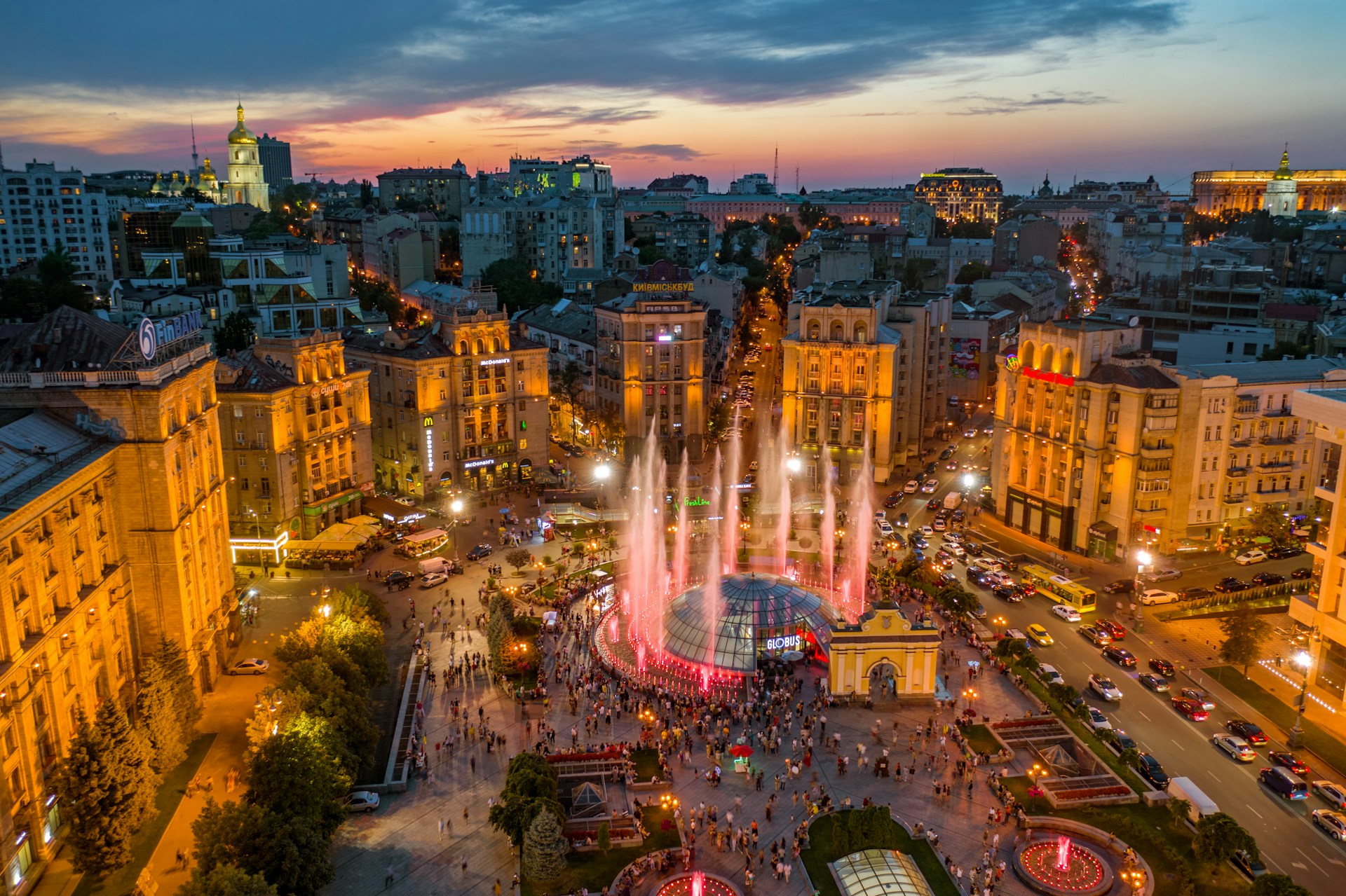 Evening view of Maidan Nezalezhnosti in Kyiv with illuminated fountains, historic buildings, and crowds of tourists exploring one of the city’s top walking route locations.