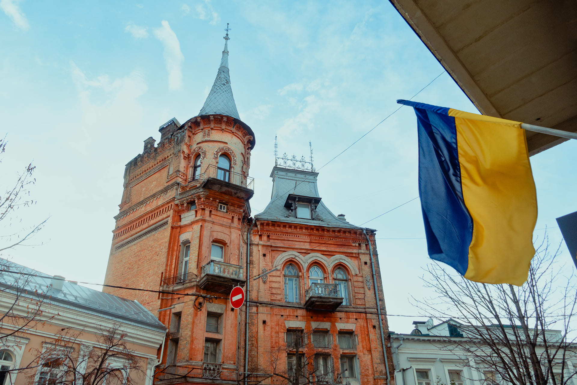 House of the Baron in Kyiv - red brick historic mansion with decorative tower and arched windows, Ukrainian flag waving against a blue sky