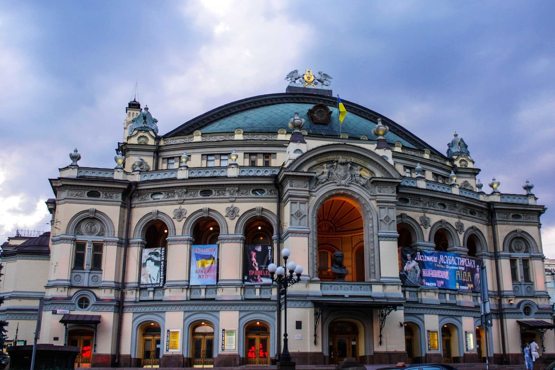 National Opera House in Kyiv - historic opera house with ornate facade and arched entrance, illuminated in the evening under a dramatic cloudy sky