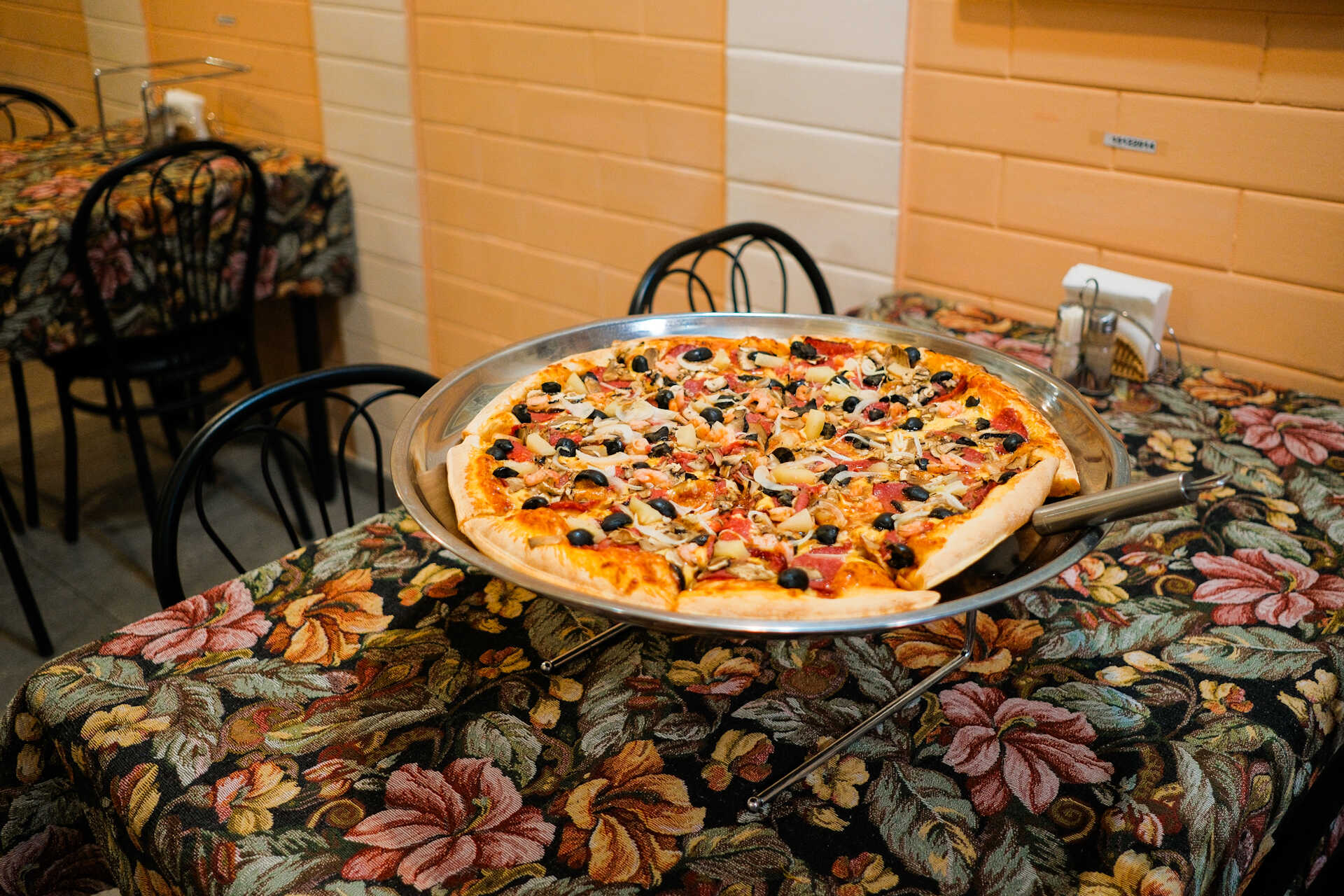 Large supreme pizza with black olives on a floral table at Vesuvio