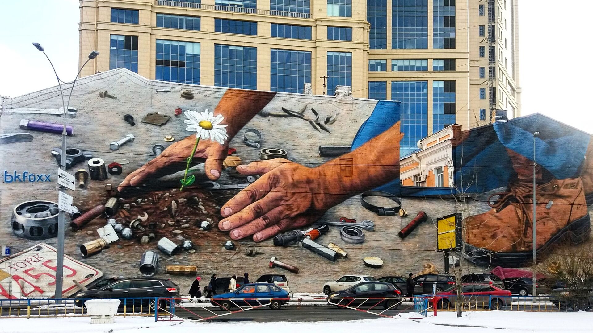 "Rise from the dirt" mural in Kyiv - large street mural showing hands protecting a small flower growing from soil among scattered tools and metal parts