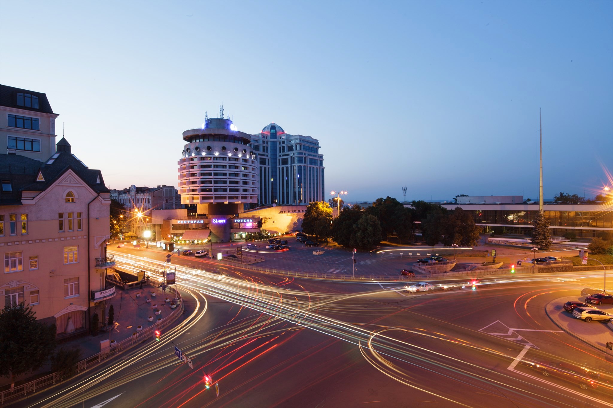 Salute Hotel in Kyiv - evening cityscape with the cylindrical hotel building illuminated, long-exposure light trails of traffic at a busy intersection