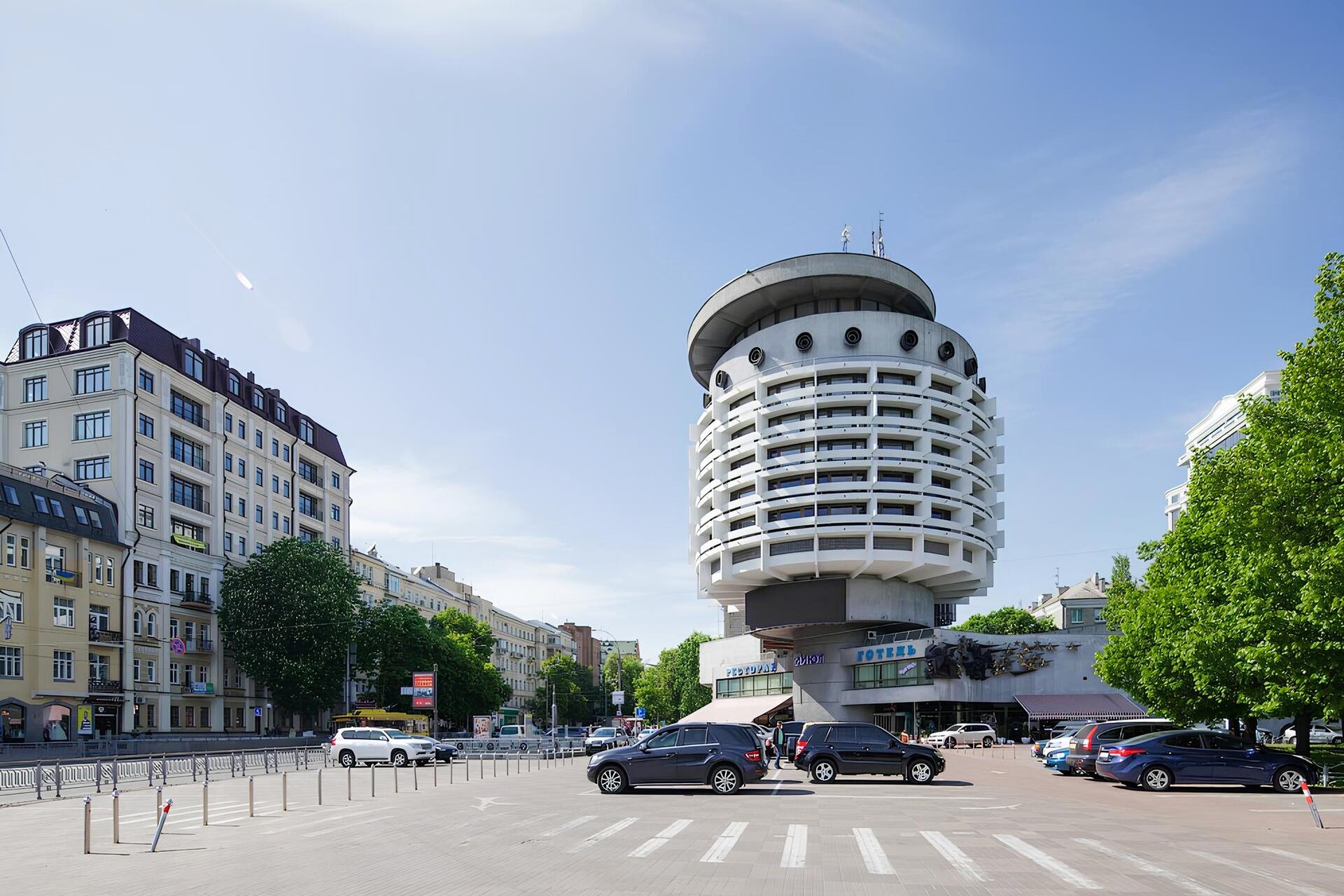 Salute Hotel in Kyiv - cylindrical modernist hotel building on a sunny day, surrounded by cars and city streets
