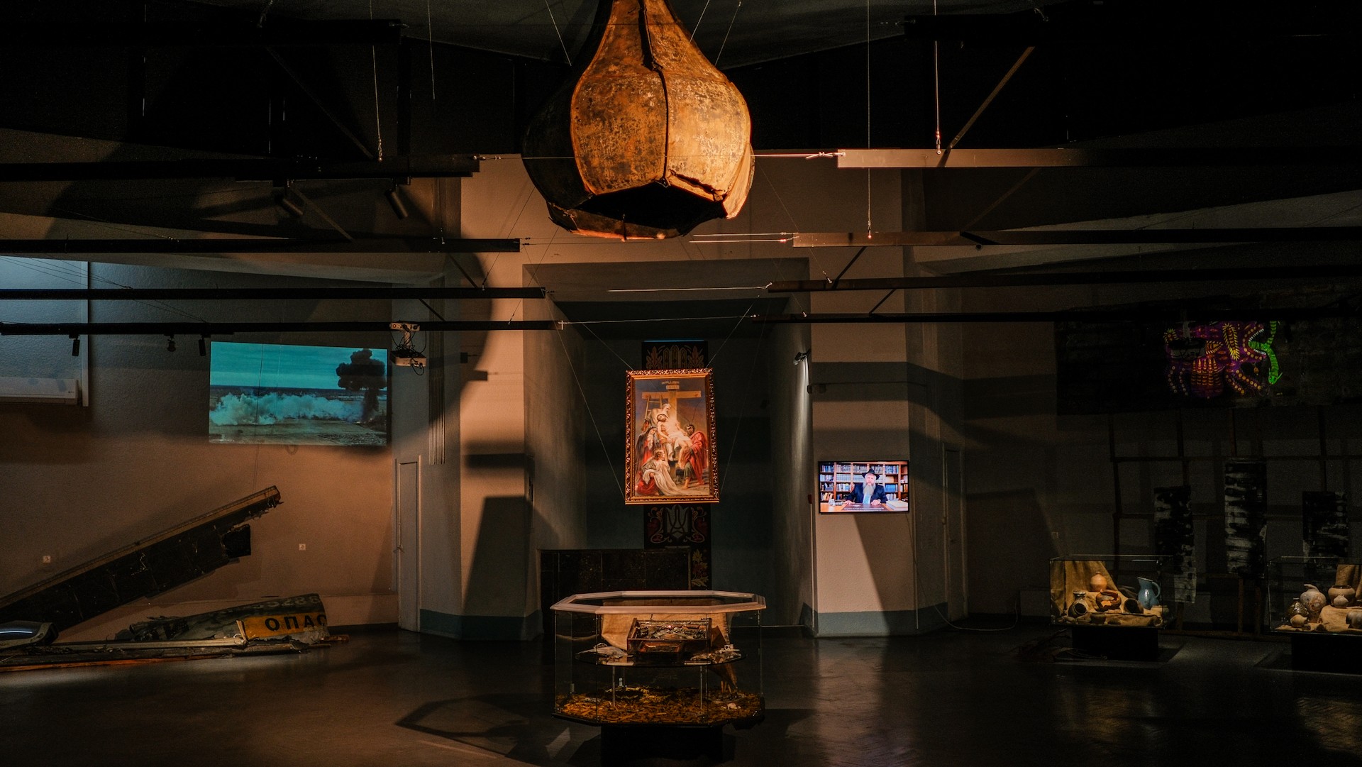 War Museum in Kyiv - dark exhibition hall with a suspended damaged church dome, a religious icon, and war artifacts