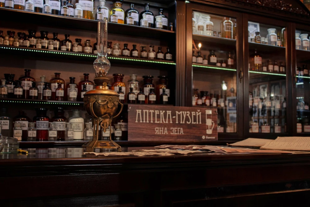 Pharmacy Museum in Kyiv - close-up of a wooden counter featuring a vintage kerosene lamp and a sign reading "Jan Zeh Pharmacy Museum" amidst glass bottles