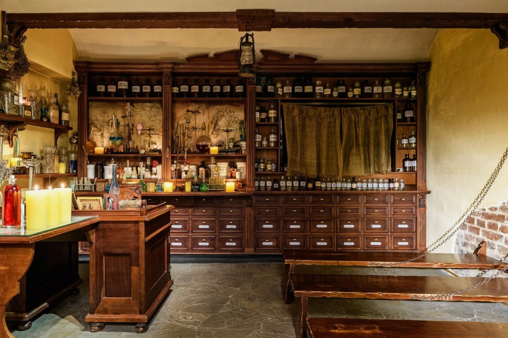 Pharmacy Museum in Kyiv - atmospheric interior of the apothecary featuring stone floors, dark wooden furniture filled with bottles, and candlelight creating a mysterious mood
