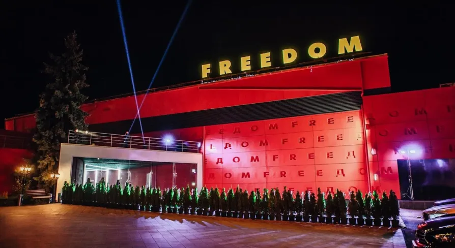 Freedom Hall in Kyiv - bright red facade with yellow neon letters and spotlights beaming into the night sky
