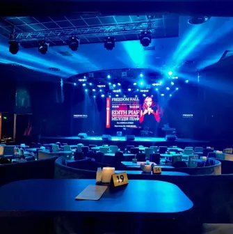 Freedom Hall in Kyiv - cozy concert hall bathed in blue light with round tables and a stage prepared for a show