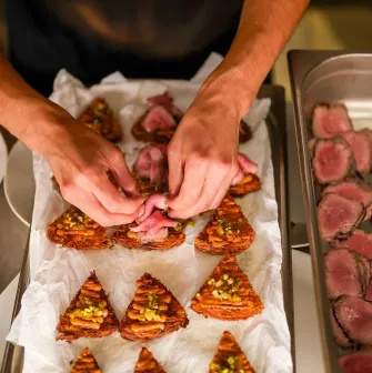 Chef's hands adding slices of meat to appetizers on a tray in a restaurant
