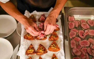 Chef's hands adding slices of meat to appetizers on a tray in a restaurant