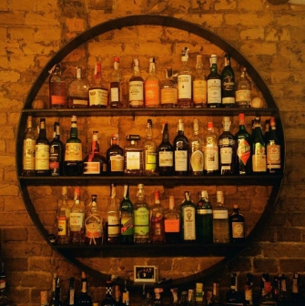 Bar Restaurant Kosatka - circular shelving unit filled with bottles of liquor against a brick wall