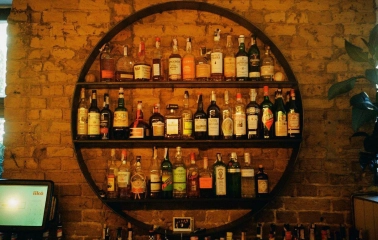 Bar Restaurant Kosatka - circular shelving unit filled with bottles of liquor against a brick wall