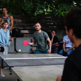 Kashtan - people playing table tennis on an outdoor patio surrounded by greenery