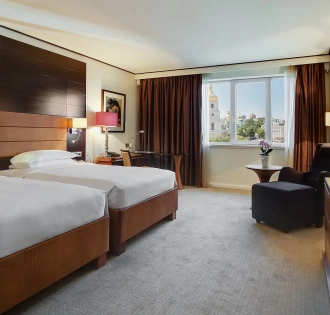 Room with two twin beds at the Hyatt Regency Kyiv with a work desk and an armchair by the window