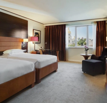 Room with two twin beds at the Hyatt Regency Kyiv with a work desk and an armchair by the window