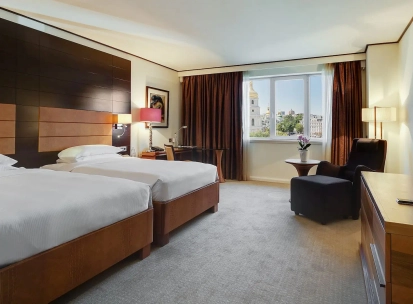 Room with two twin beds at the Hyatt Regency Kyiv with a work desk and an armchair by the window