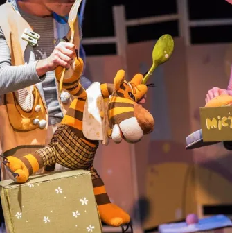 Kyiv Academic Puppet Theatre in Kyiv - close-up stage scene featuring a plush tiger puppet being manipulated by actors in costumes holding giant spoons