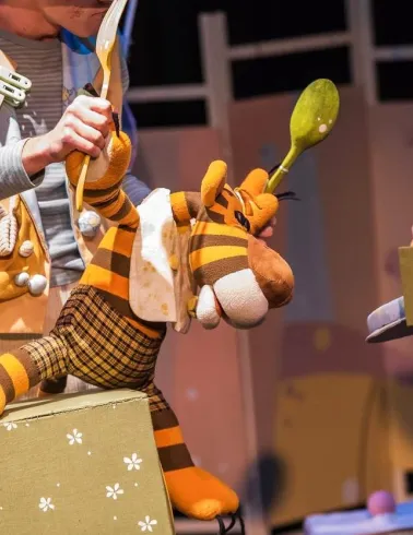 Kyiv Academic Puppet Theatre in Kyiv - close-up stage scene featuring a plush tiger puppet being manipulated by actors in costumes holding giant spoons