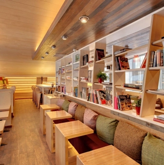 One Love Coffee in Kyiv - row of wooden tables along bookshelf with red wire lamps