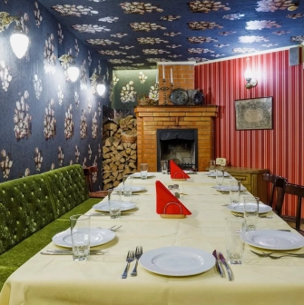 Restaurant Za Dvoma Zaicyamy - long dining table set in a room with a fireplace woodpile and patterned walls