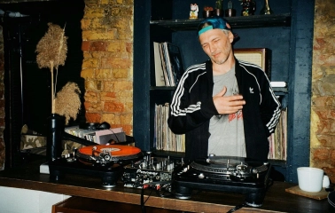 Bar Restaurant Kosatka - man posing in front of two turntables and a shelf with records