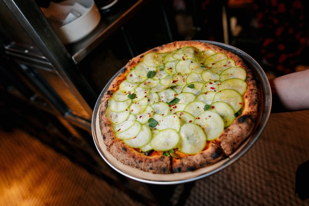 Pizza with thinly sliced cucumber and spices at Italiiska redaktsiia