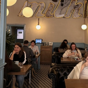 Milk Bar - cozy cafe interior with guests enjoying coffee under neon milk sign