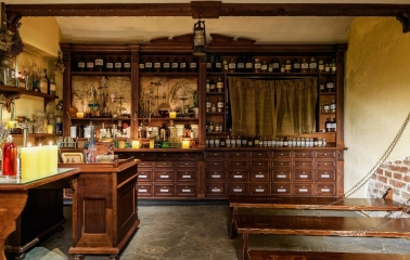 Pharmacy Museum in Kyiv - atmospheric interior of the apothecary featuring stone floors, dark wooden furniture filled with bottles, and candlelight creating a mysterious mood