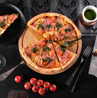 A cut pizza on a wooden board with cherry tomatoes and sauce