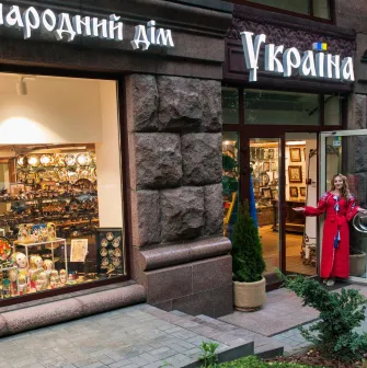 Narodnyi Dim Ukraina in Kyiv - exterior view of the shop entrance with a stone facade and a woman in a red vyshyvanka welcoming visitors