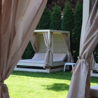 Soft bed loungers with beige curtains and a wooden frame on green grass