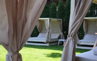 Soft bed loungers with beige curtains and a wooden frame on green grass