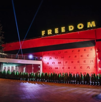 Freedom Hall in Kyiv - bright red facade with yellow neon letters and spotlights beaming into the night sky