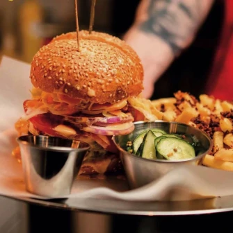 True Burger Bar - close-up of a plated gourmet burger served with fries and pickles