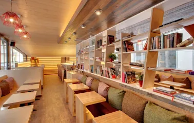 One Love Coffee in Kyiv - row of wooden tables along bookshelf with red wire lamps