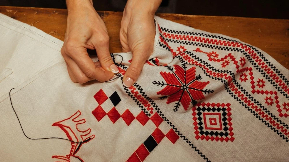 Hands embroidering a traditional red and black pattern on fabric
