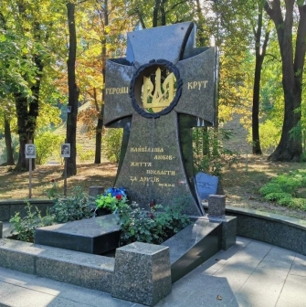 Askoldova Mohyla in Kyiv - solemn black granite memorial cross dedicated to the Heroes of Kruty featuring a golden trident wreath amidst the park greenery