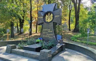 Askoldova Mohyla in Kyiv - solemn black granite memorial cross dedicated to the Heroes of Kruty featuring a golden trident wreath amidst the park greenery
