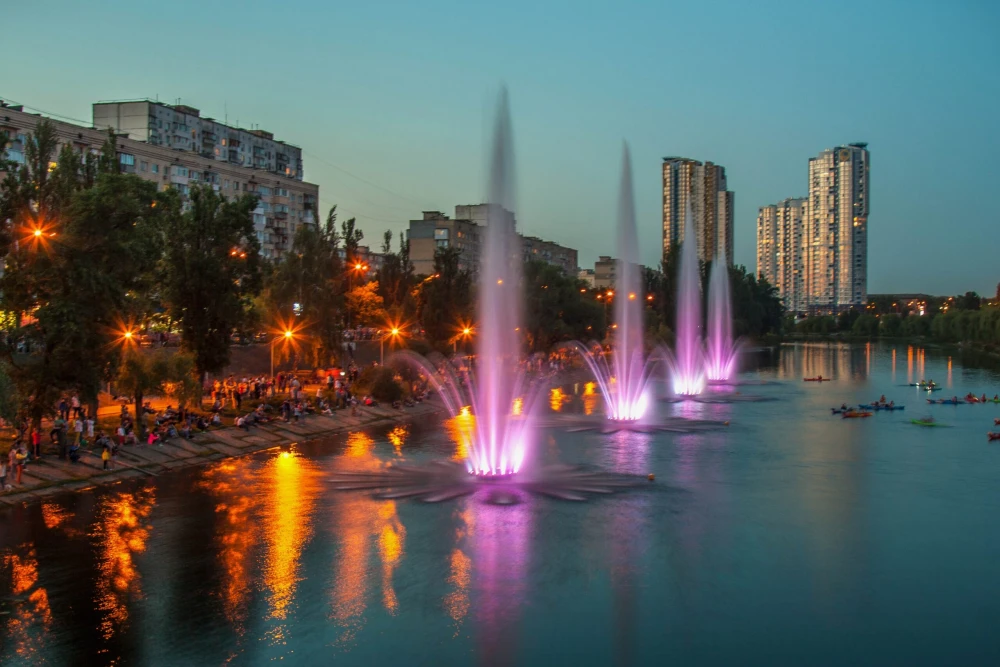Rusanivska Naberezhna in Kyiv - vibrant evening scene featuring a row of illuminated purple and pink fountains spraying high into the air