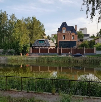 Park Kyn-Grust - view across a pond with green reeds towards private brick mansions behind a fence