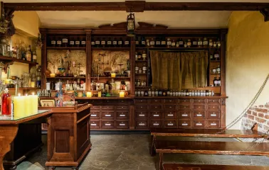 Pharmacy Museum in Kyiv - atmospheric interior of the apothecary featuring stone floors, dark wooden furniture filled with bottles, and candlelight creating a mysterious mood