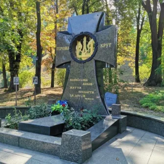 Askoldova Mohyla in Kyiv - solemn black granite memorial cross dedicated to the Heroes of Kruty featuring a golden trident wreath amidst the park greenery