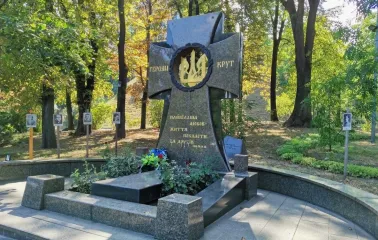 Askoldova Mohyla in Kyiv - solemn black granite memorial cross dedicated to the Heroes of Kruty featuring a golden trident wreath amidst the park greenery