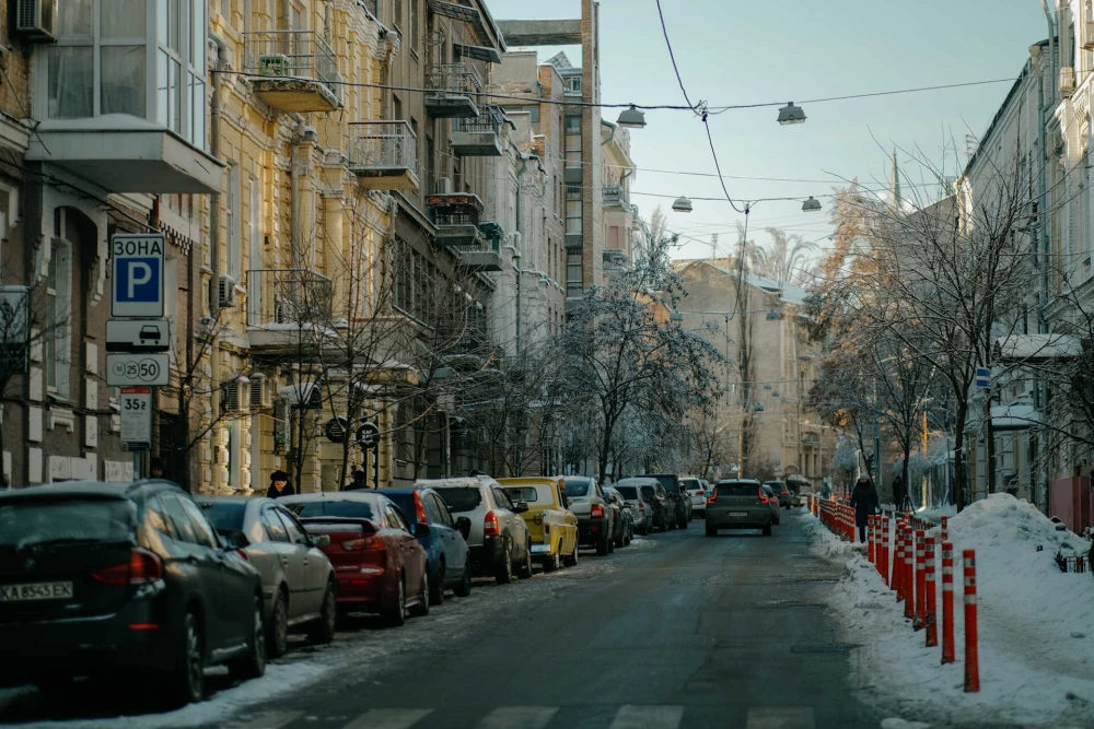 Cars parked along a snowy street with historic buildings in Kyiv
