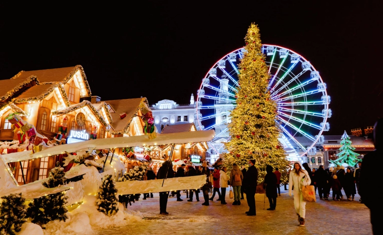 Christmas fair on Kontraktova Square in Kyiv - festive market with a large illuminated Christmas tree, Ferris wheel, and visitors walking among decorated wooden stalls at night
