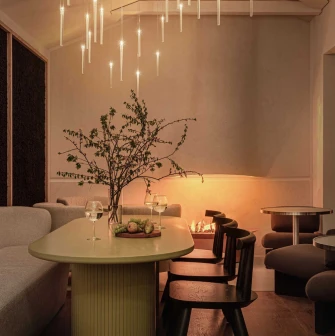 Dinner setting under multiple modern linear pendant lights creating a warm glow