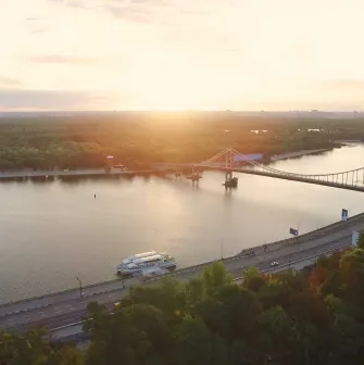 Панорамний вид на річку, міст і зелені береги на заході сонця в Гідропарку
