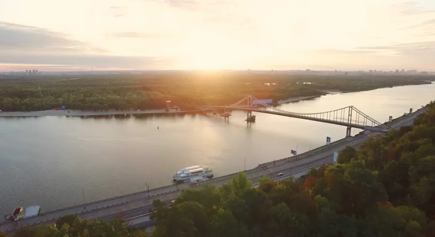 Панорамний вид на річку, міст і зелені береги на заході сонця в Гідропарку