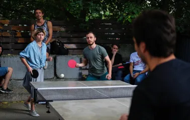 Kashtan - people playing table tennis on an outdoor patio surrounded by greenery