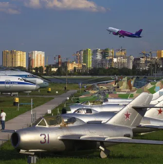 Aviation Museum in Kyiv - row of vintage silver military jets parked on the grass with a modern Wizz Air passenger plane taking off in the blue sky